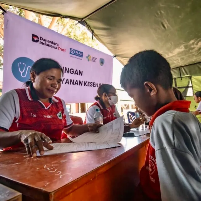 A smiling health worker goes over a form with a young boy at a health service desk